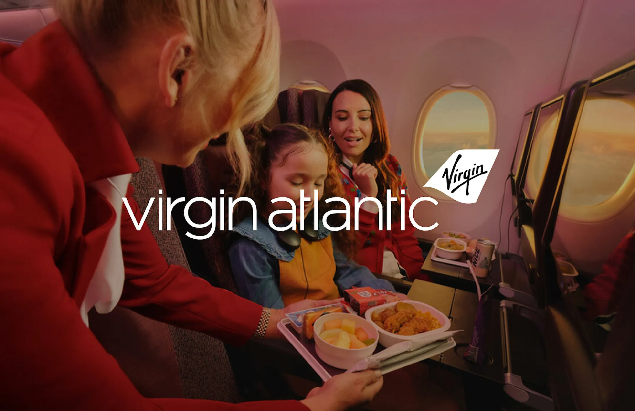 Woman and child on a flight looking at a meal held out by a flight attendant, with "Virgin Atlantic" logo overlaid.