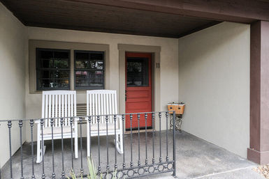Cozy covered front porch with a red door, two white rocking chairs and a decorative wrought-iron railing
