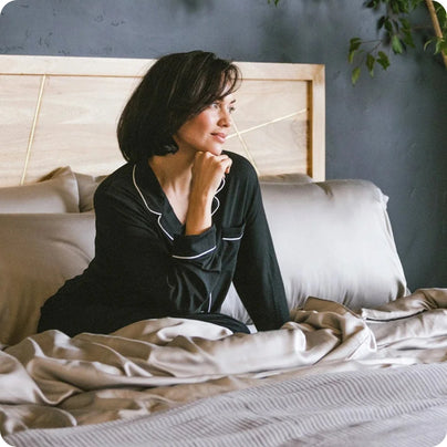 A woman in black Cozy Earth pajamas, sitting in a bed with Cozy Earth sheets.