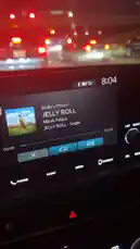 This video shows a close-up of a car's infotainment screen at night. The screen displays 'Jelly Roll' by Micah Palace playing via Bluetooth from 'Mellie's Phone'. The time on the screen changes from 8:04 to 8:05 as the song progresses. In the background, the red glow of taillights indicates the car is stuck in traffic. by @mahreen0182 with mahreen0182 by Original Sound