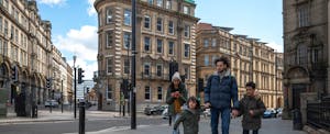 A family with two young children holds hands as they walk down a city street together.