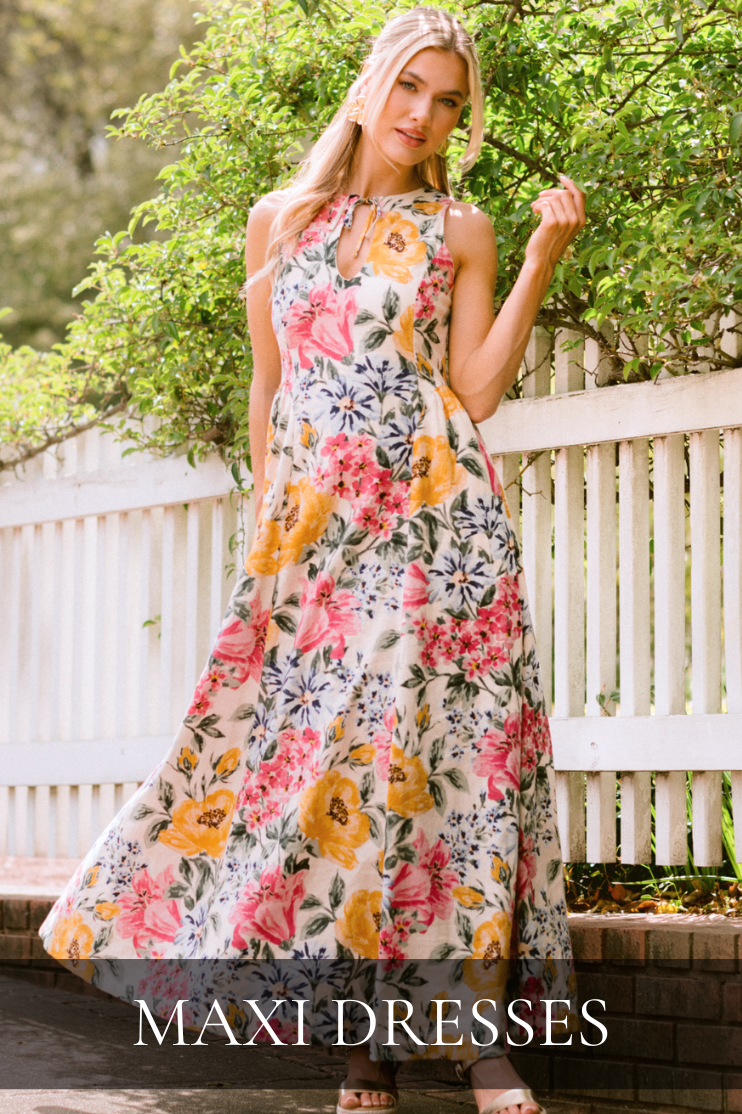 Model wearing a flowy floral maxi dress outdoors by a white fence. Dress is featured in our Maxi Dresses Collection.